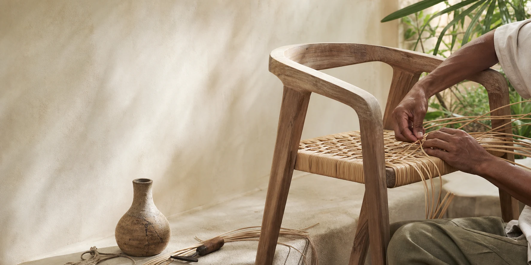 Artisan weaving natural rattan into a handcrafted teak chair
